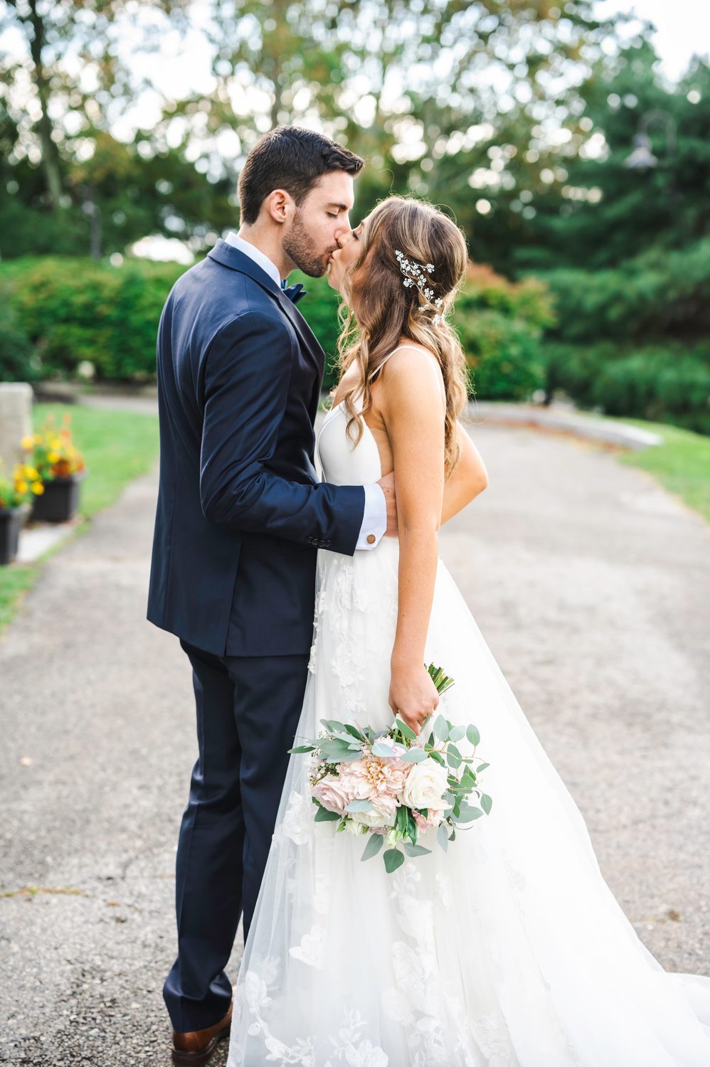 Bride and groom kissing on a garden path, bride holding a blush bouquet